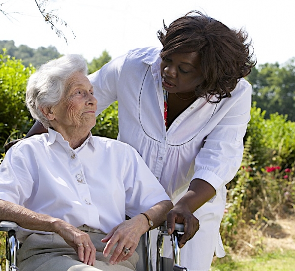 Afro-american caregiver talking to disabled senior woman outdoors
